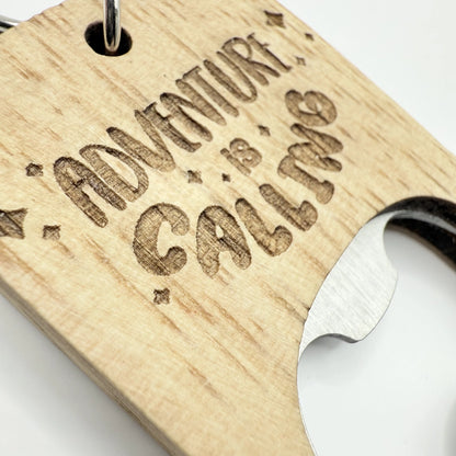 Ein hölzerner Flaschenöffner-Schlüsselanhänger mit der Aufschrift "Adventure is Calling".