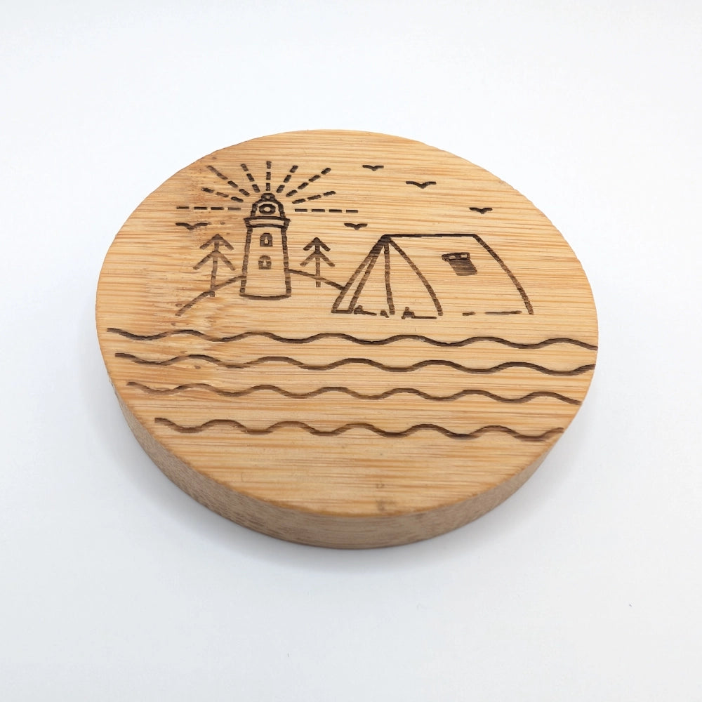 Runder Kühlschrankmagnet mit integriertem Flaschenöffner aus Bambusholz, mit einer Gravur versehen, bestehend aus einem Leuchtturm und einem Zelt.